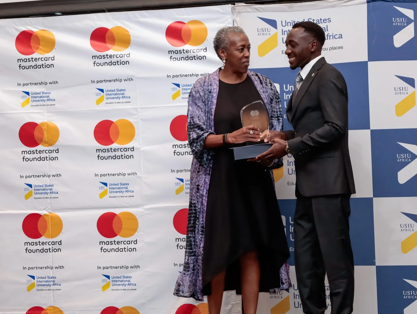 Eric receiving an award on stage beside a USIU-Africa event backdrop